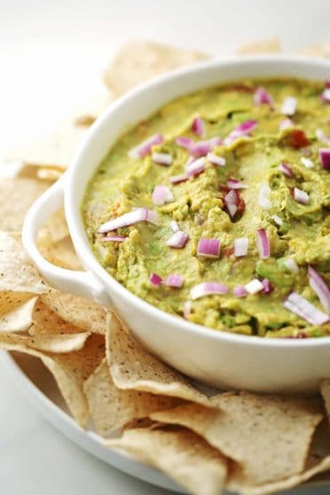 serving white bowl with green guacamole and chips