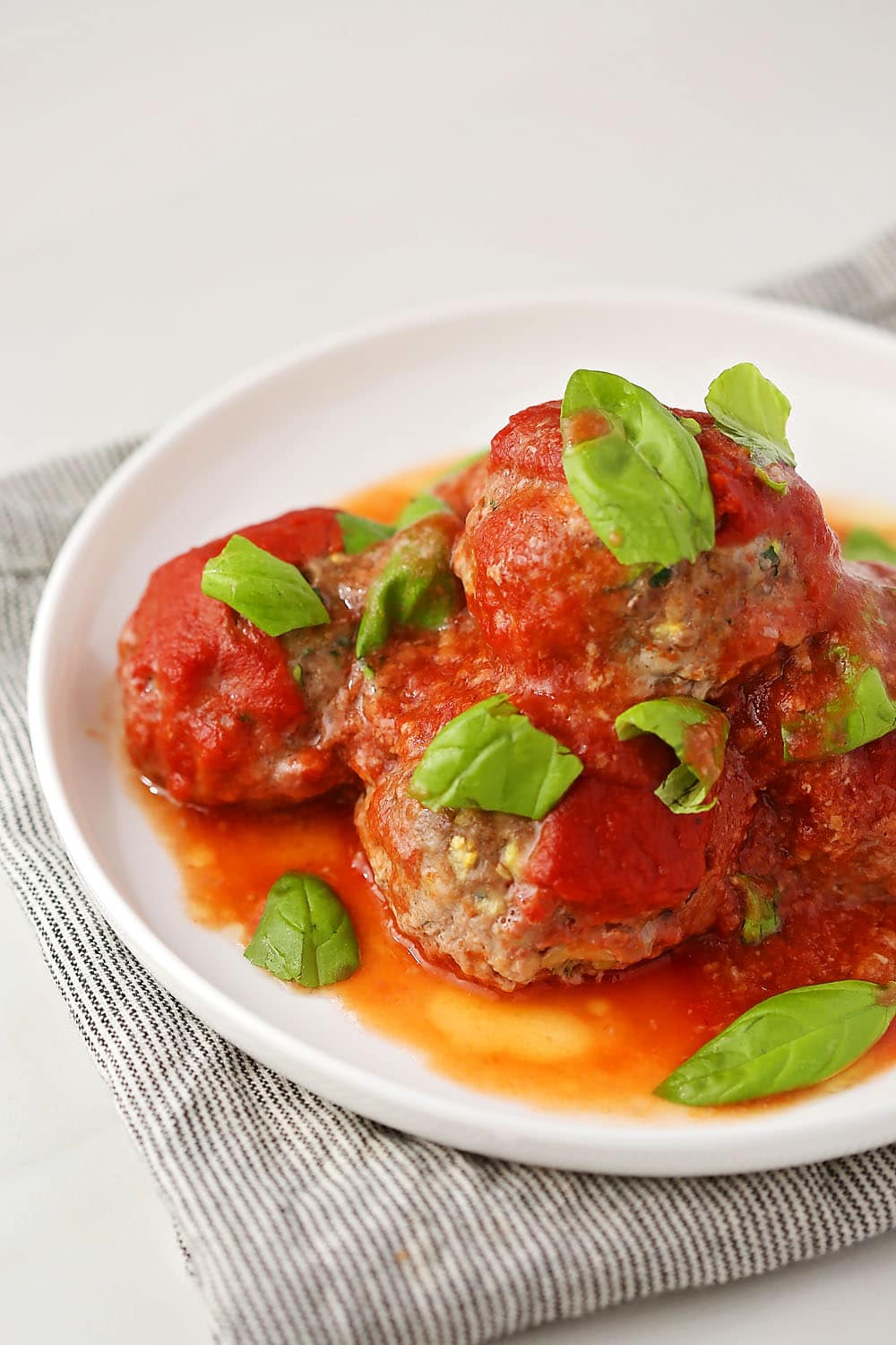 white plate with Zucchini Beef Meatballs topped with tomato sauce and fresh basil leaves