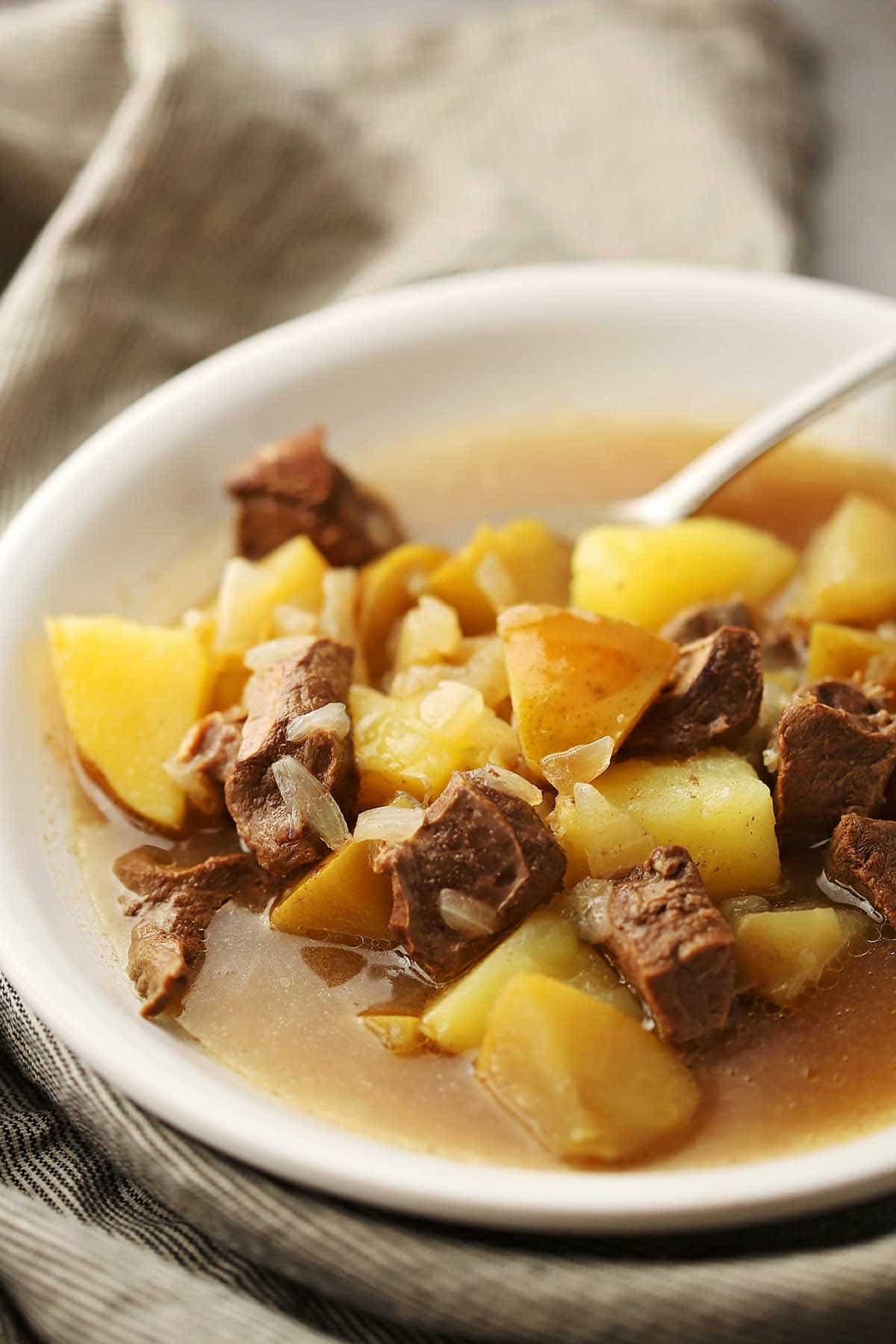white bowl with yellow potatoes, meat and brown broth