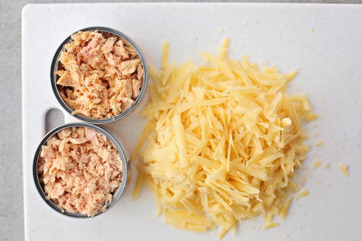 cutting board with shredded cheese and two cans of drained tuna
