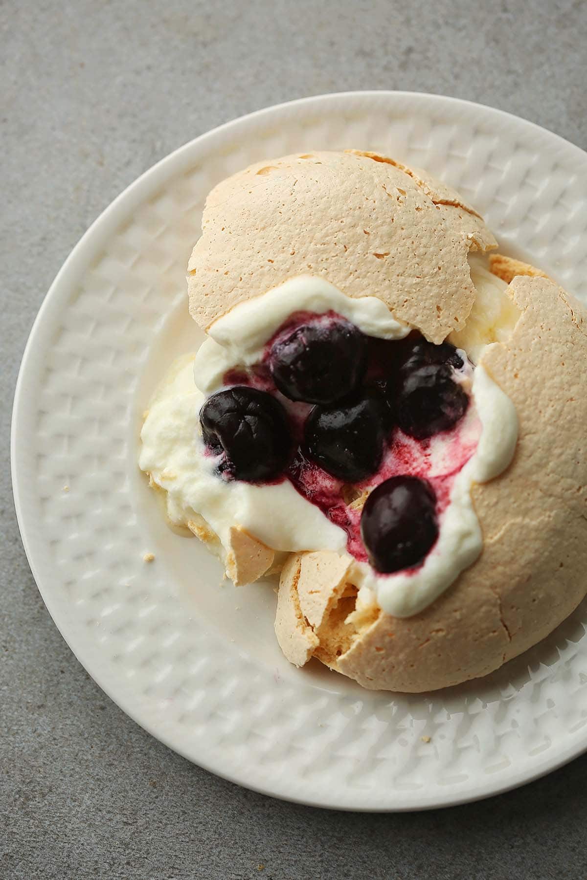 serving plate with pavlova nest, topped with white cream and dark cherries