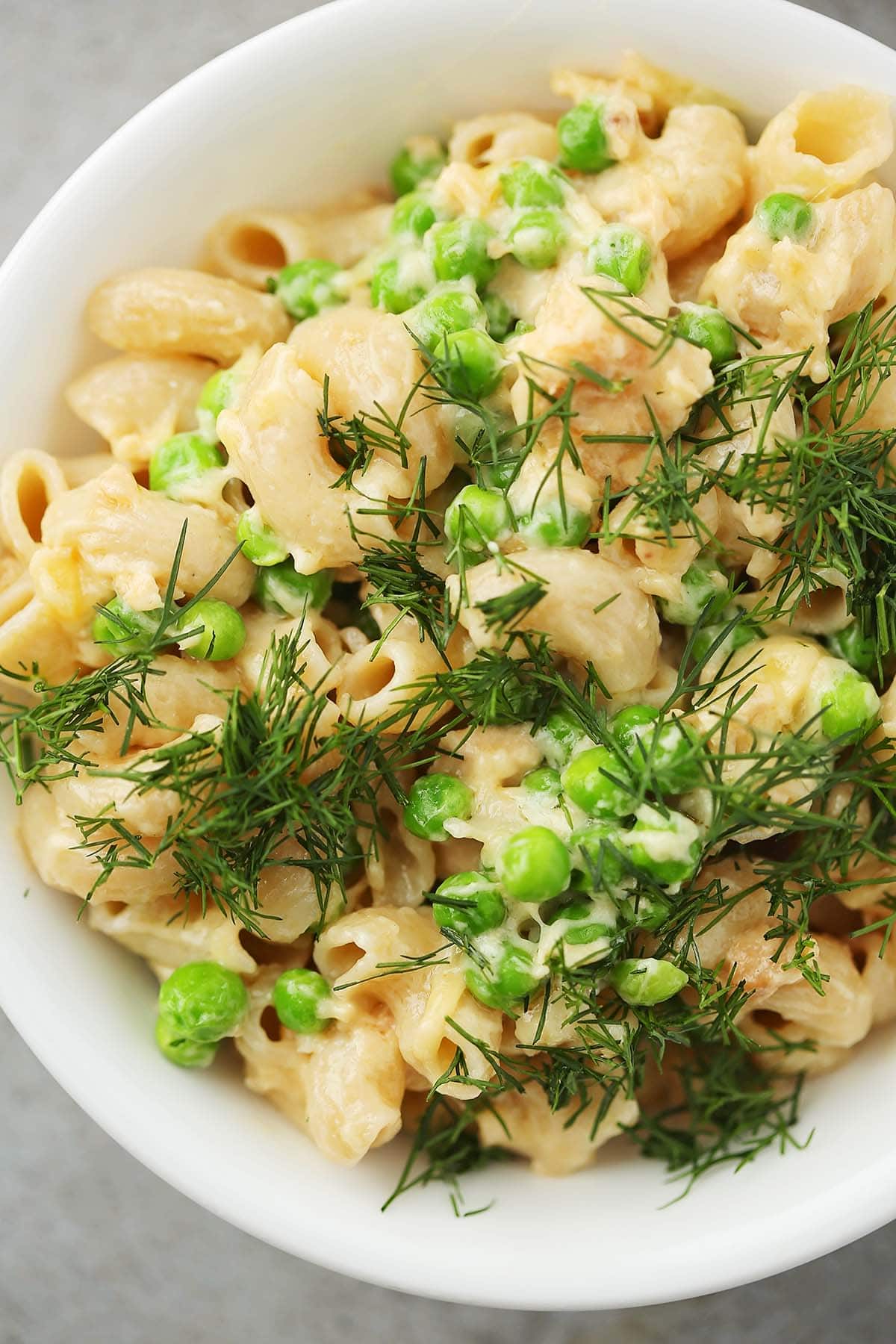 white bowl filled with pasta, peas and green garnish