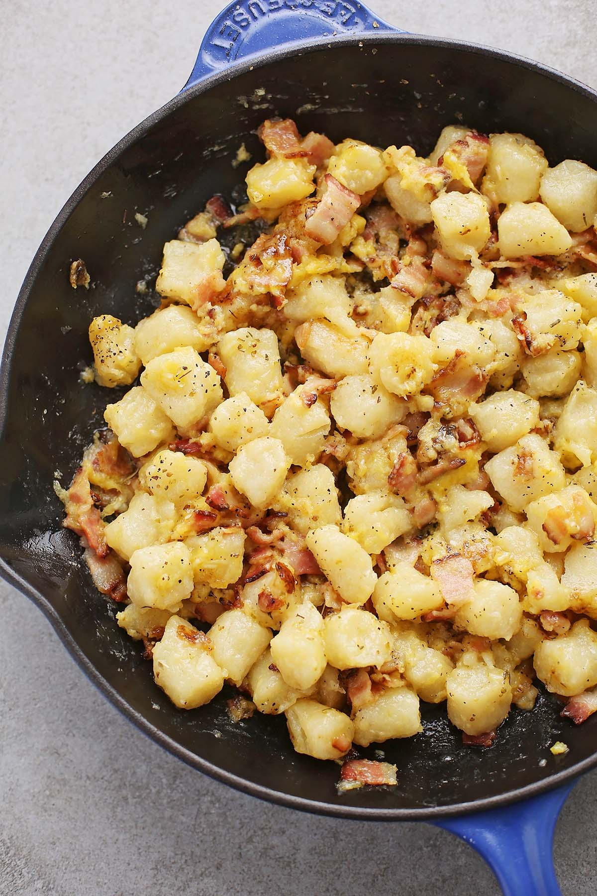 large cat iron skillet with gnocchi, bacon and yellow sauce