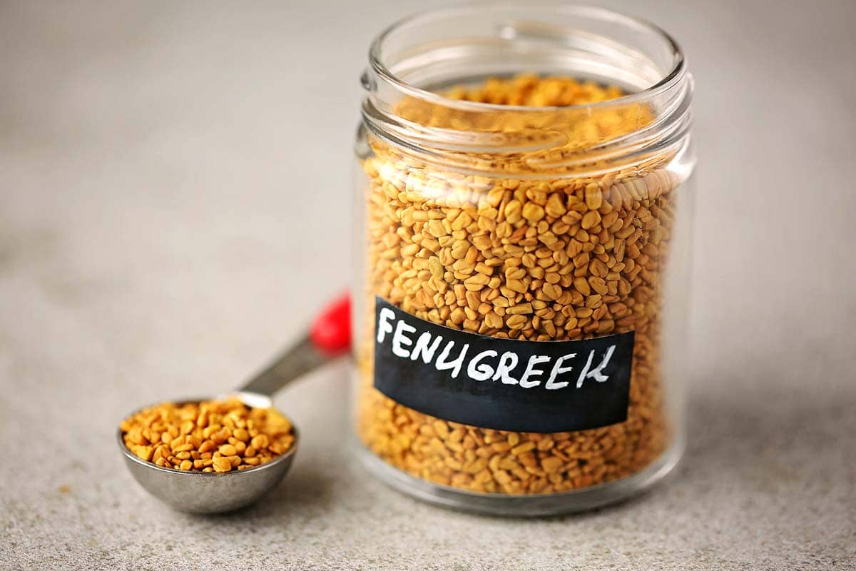 small labeled glass jar with fenugreek seeds and measuring spoon filled with seeds