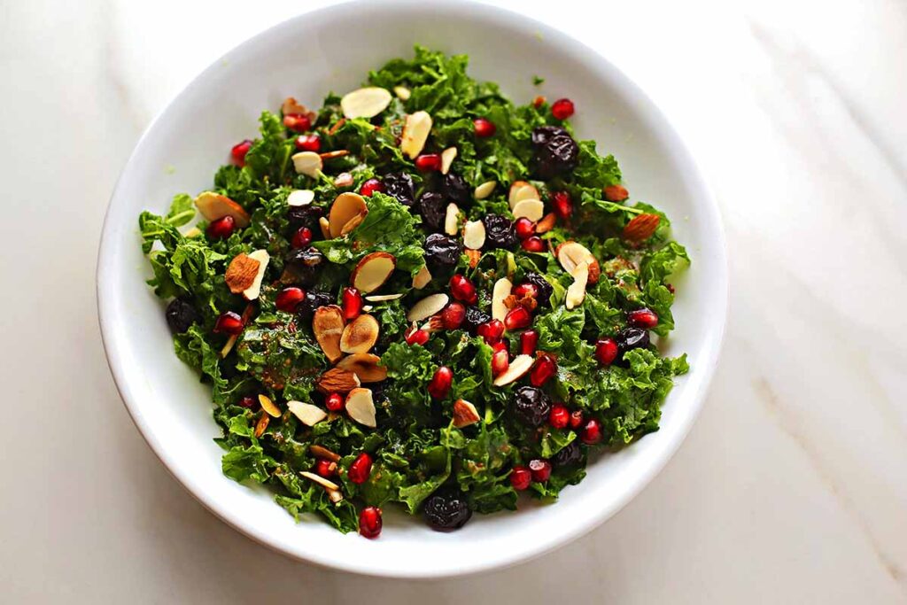 white serving plate with colorful salad with kale, pomegranate seeds, sliced almonds