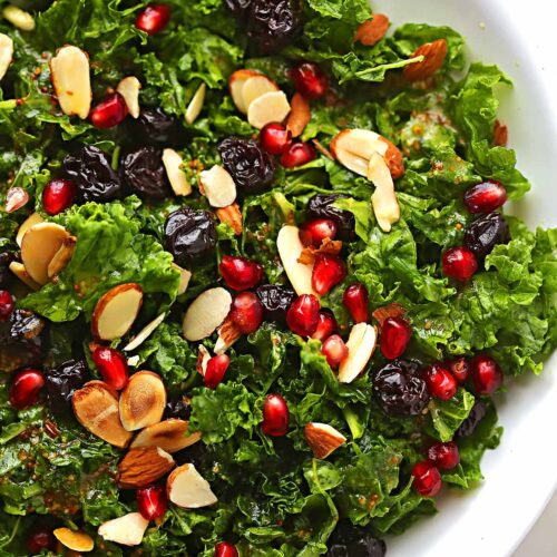 white serving plate with salad with greens, almonds, pomegranate seeds