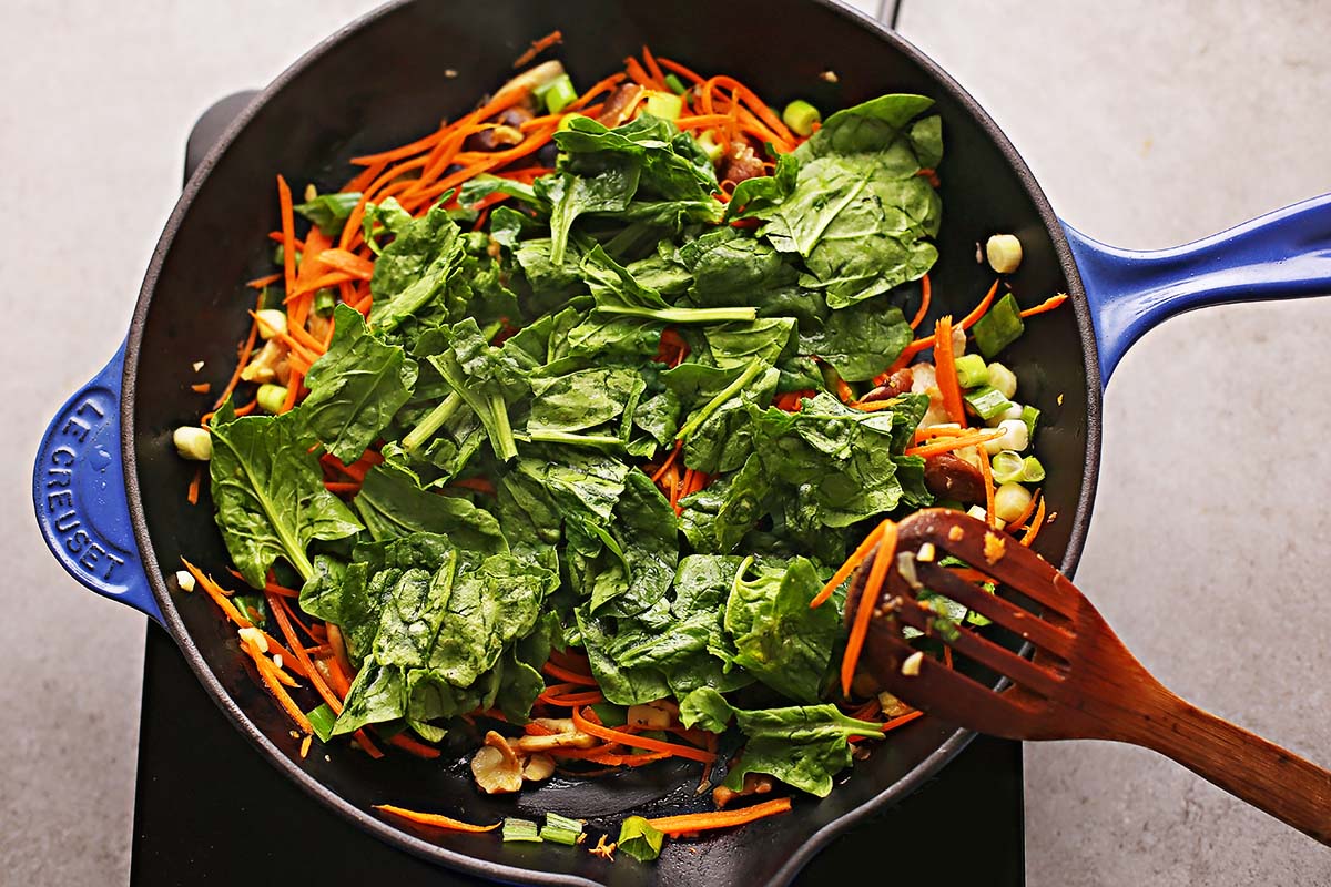 cast iron skillet with orange and green vegetables and wooden spoon