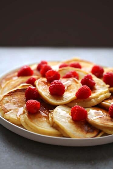 serving plate with small pancakes and fresh raspberries drizzled with maple syrup