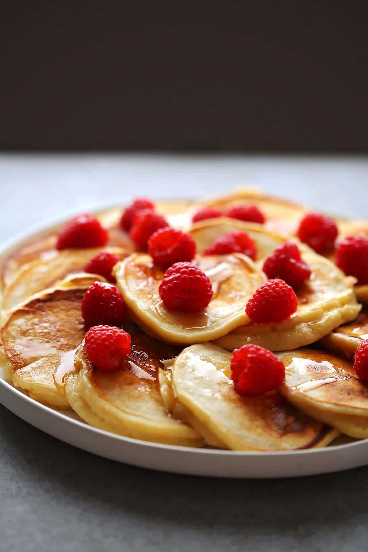 table top with large serving plate with mini pancakes and fresh raspberries