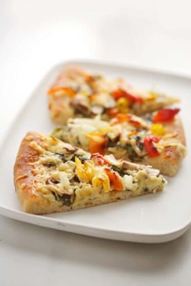 serving white plate with two slices of pizza topped with vegetables
