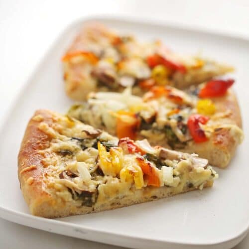 serving white plate with two slices of pizza topped with vegetables