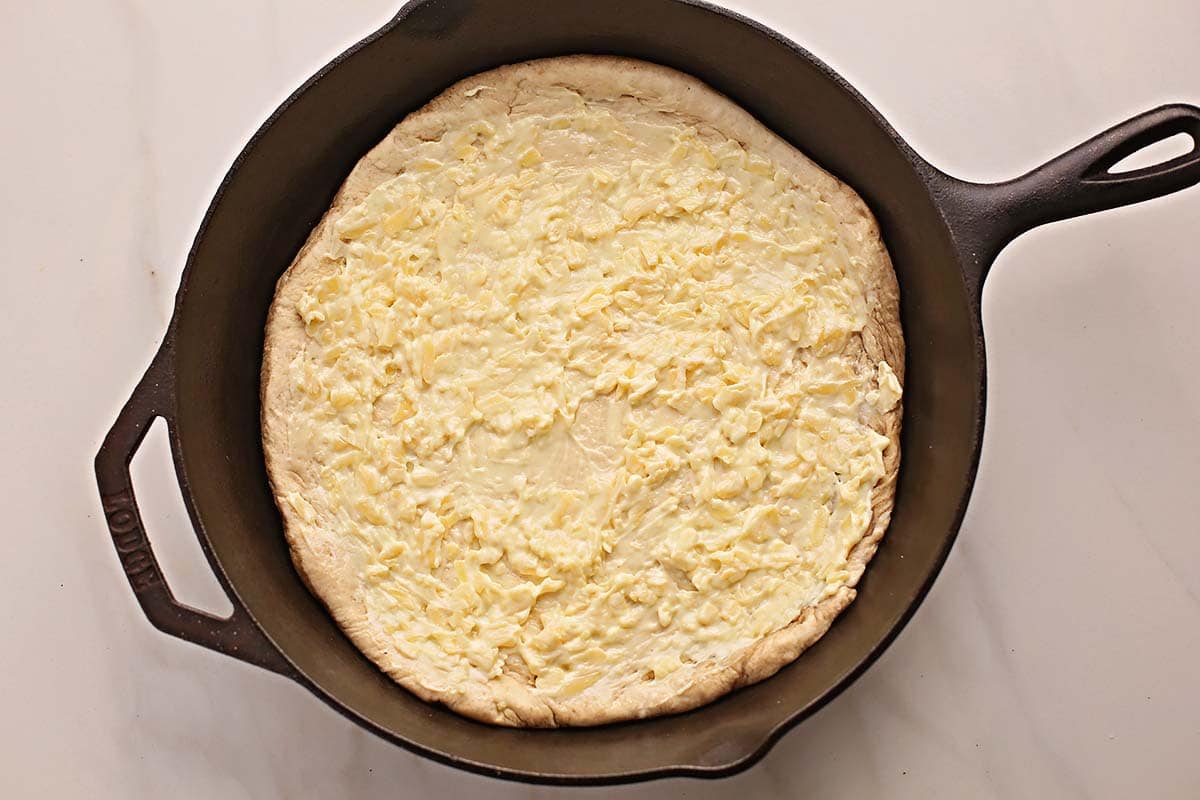 cast iron skillet with pizza dough and cheese spread