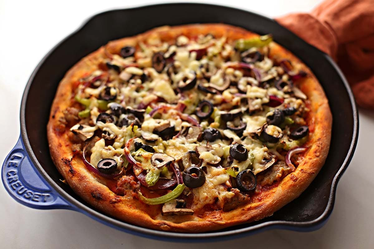 freshly baked pizza topped with black olives and cheese inside cast-iron skillet 