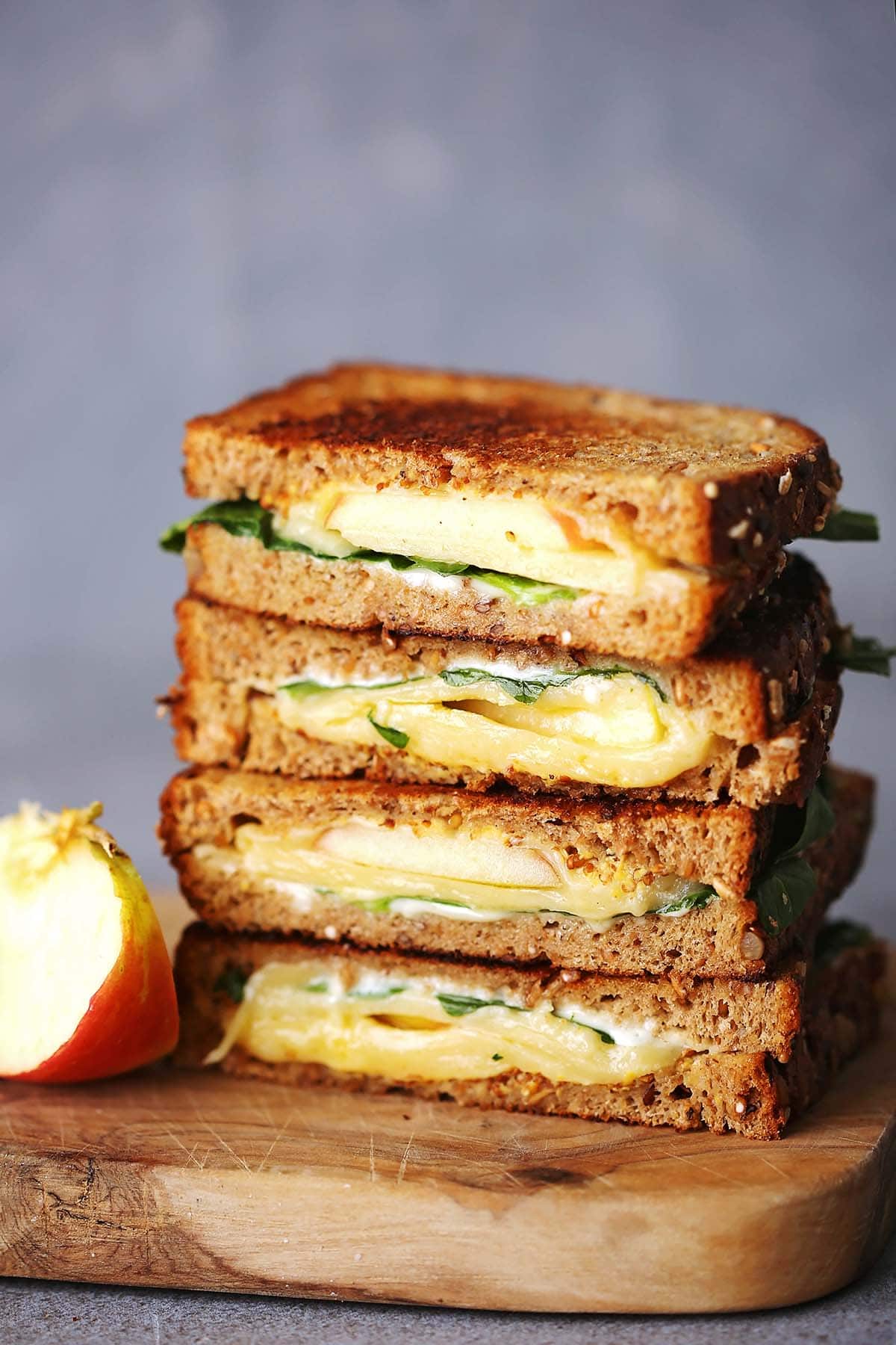 cutting board with sliced sandwich with melting cheese, apples and spinach