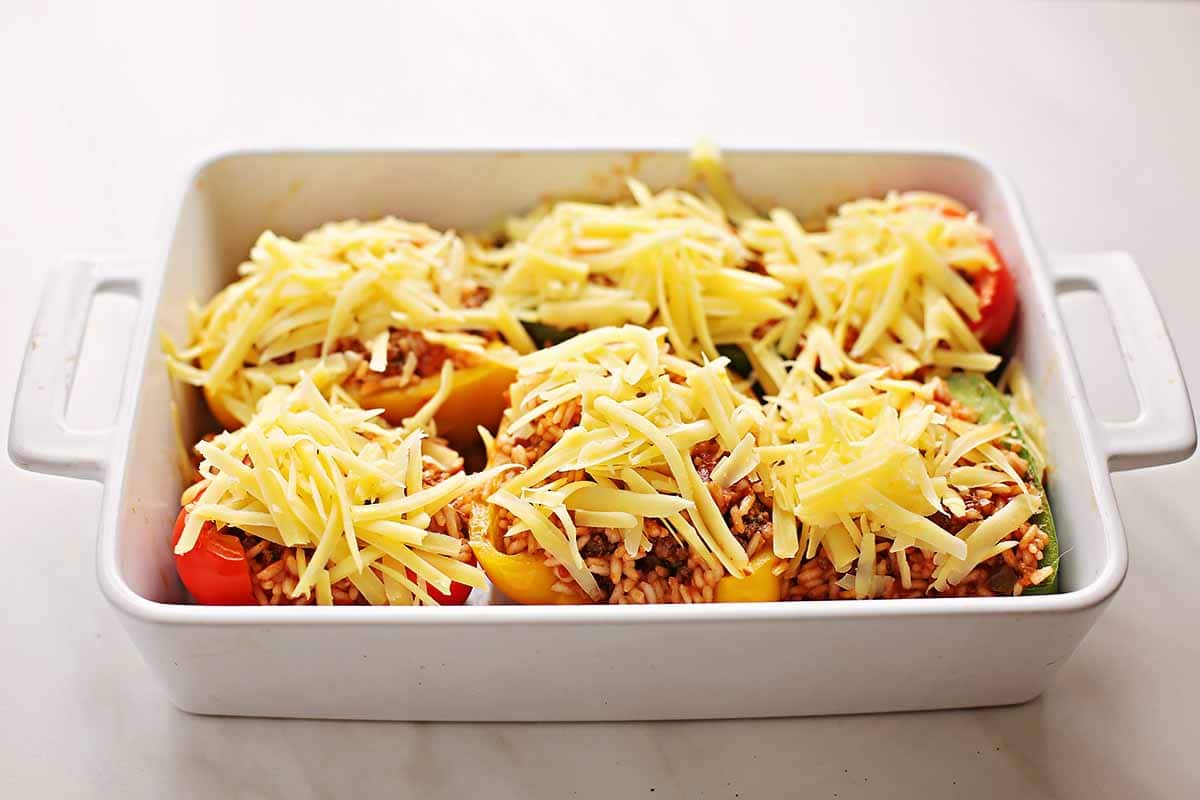 white baking dish with uncooked stuffed bell peppers topped with grated cheese