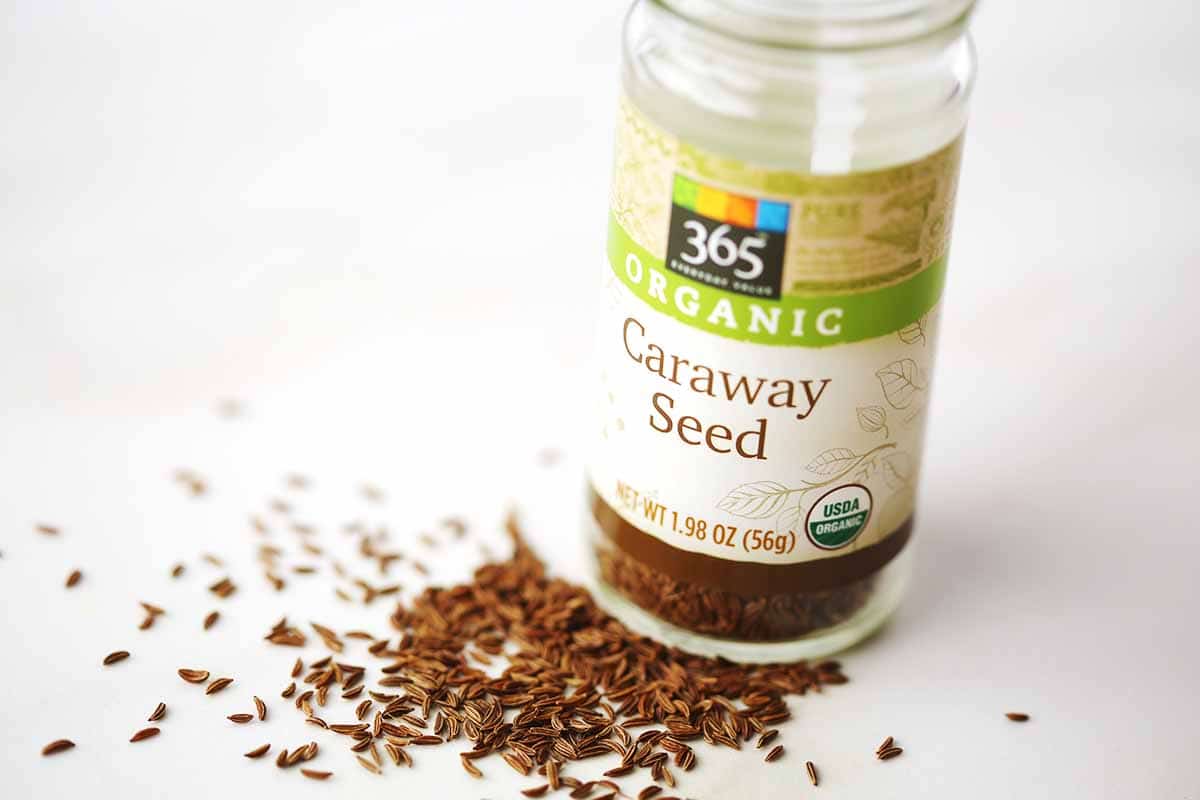table top with spilled dried brown seeds and glass jar with label "Caraway Seeds"