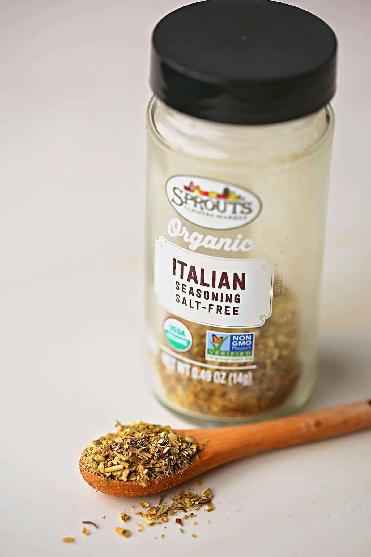 spice jar with label "italian seasoning" and small wooden teaspoon filled with dry herbs