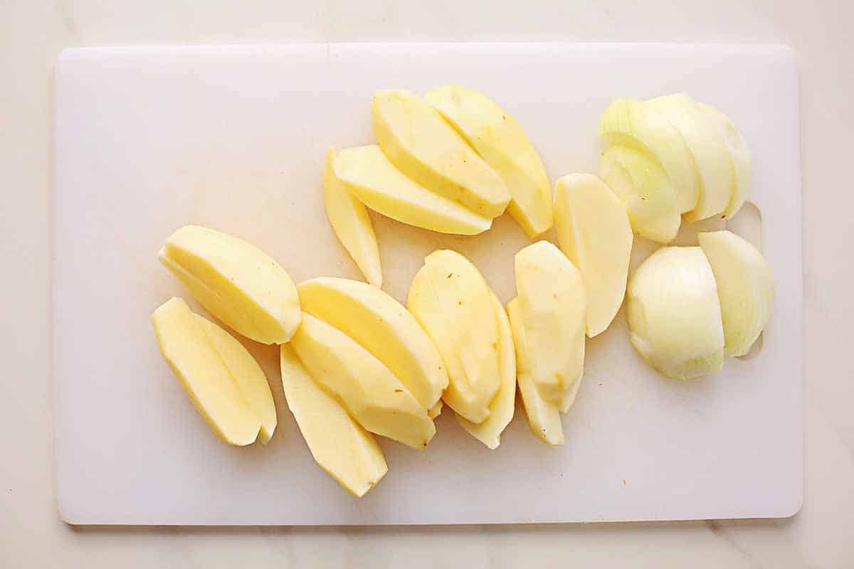 cutting board with peeled and sliced potatoes and onions