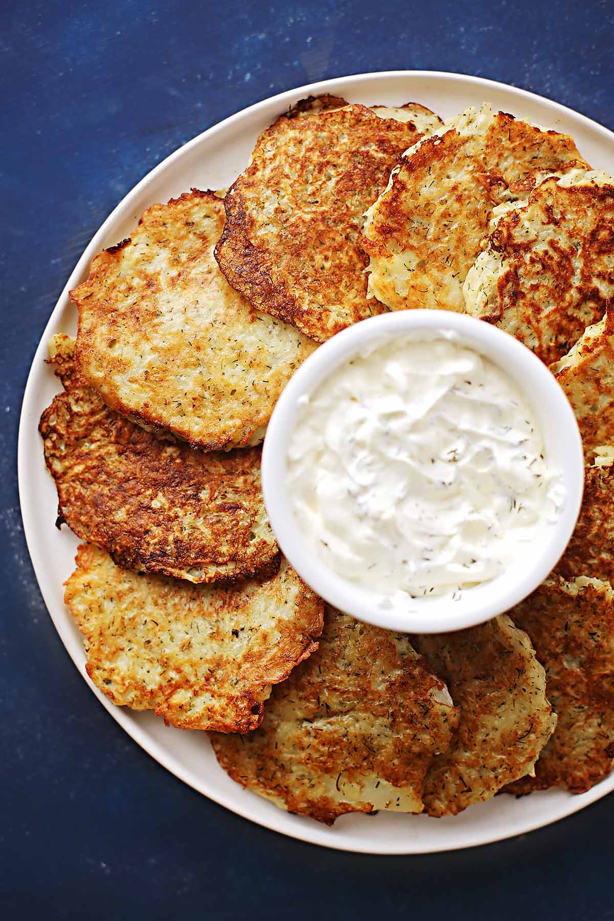white plate with fried small potato pancakes and small bowl with sour cream 