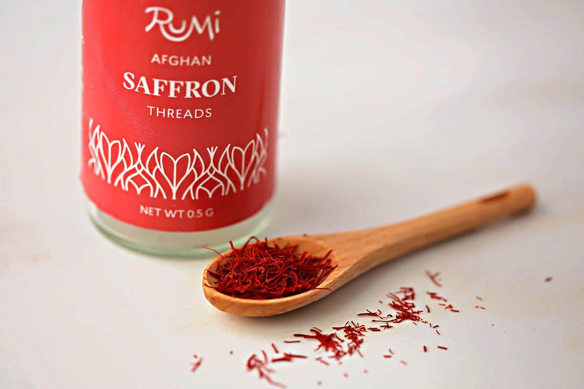 small wooden spoon filled with bright red dried spice, glass bottle with red label "afghan saffron"
