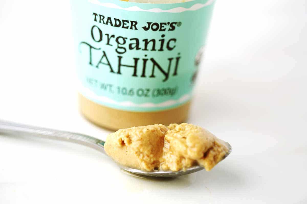 spoon filled with tahini paste, glass jar labeled "tahini".