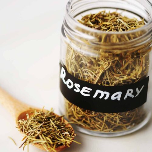 glass jar filled with dried spice with label "rosemary", teaspoon filled with dried brown spice