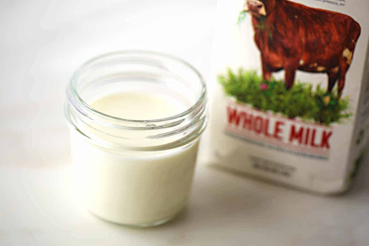 mason jar filled with white milk, carton of milk with image of the cow and label "whole milk"