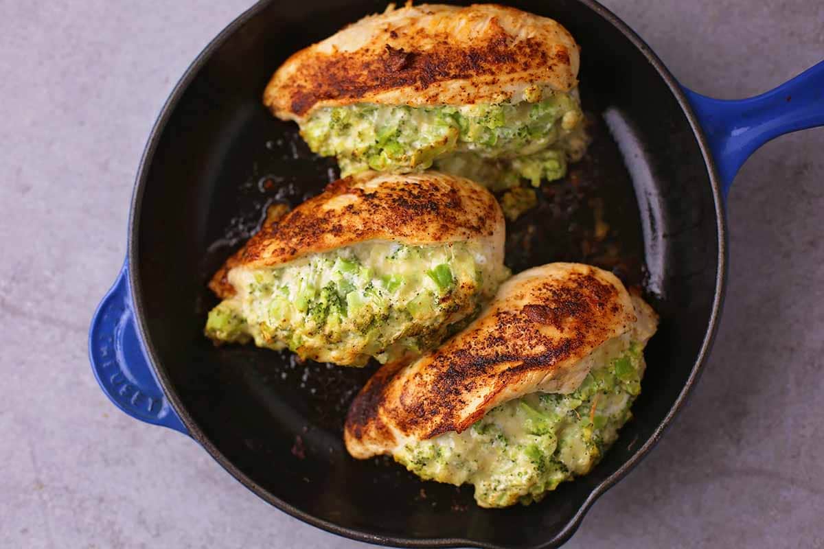 cast iron skillet with roasted chicken breasts with melted green-colored stuffing inside