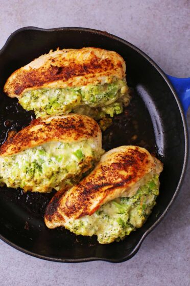 vertical close up shot of cast iron pan with cooked chicken breast filled with broccoli and cheese mix