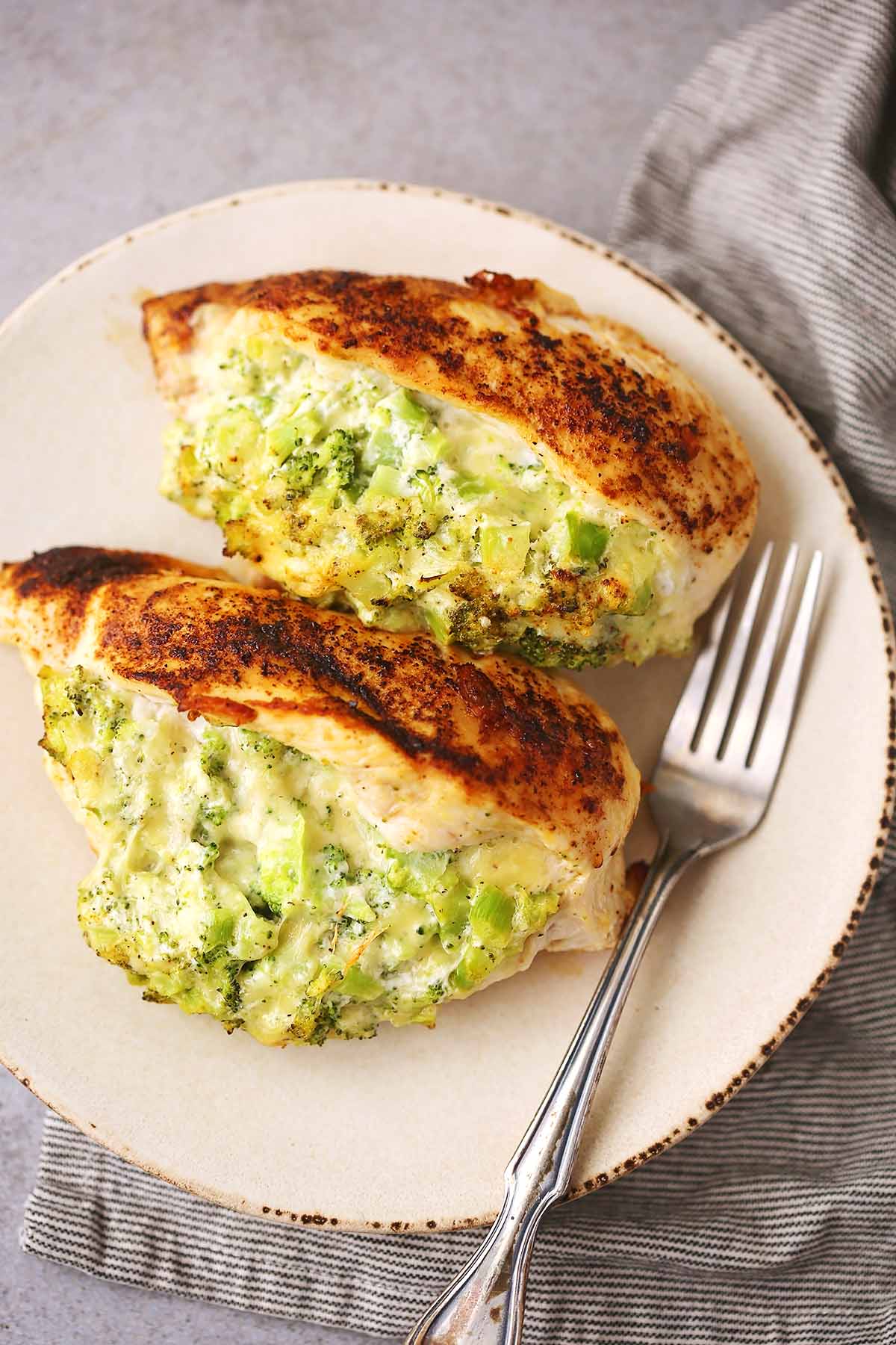 white serving plate with two cooked chicken breasts filled with melted cheese and broccoli filling