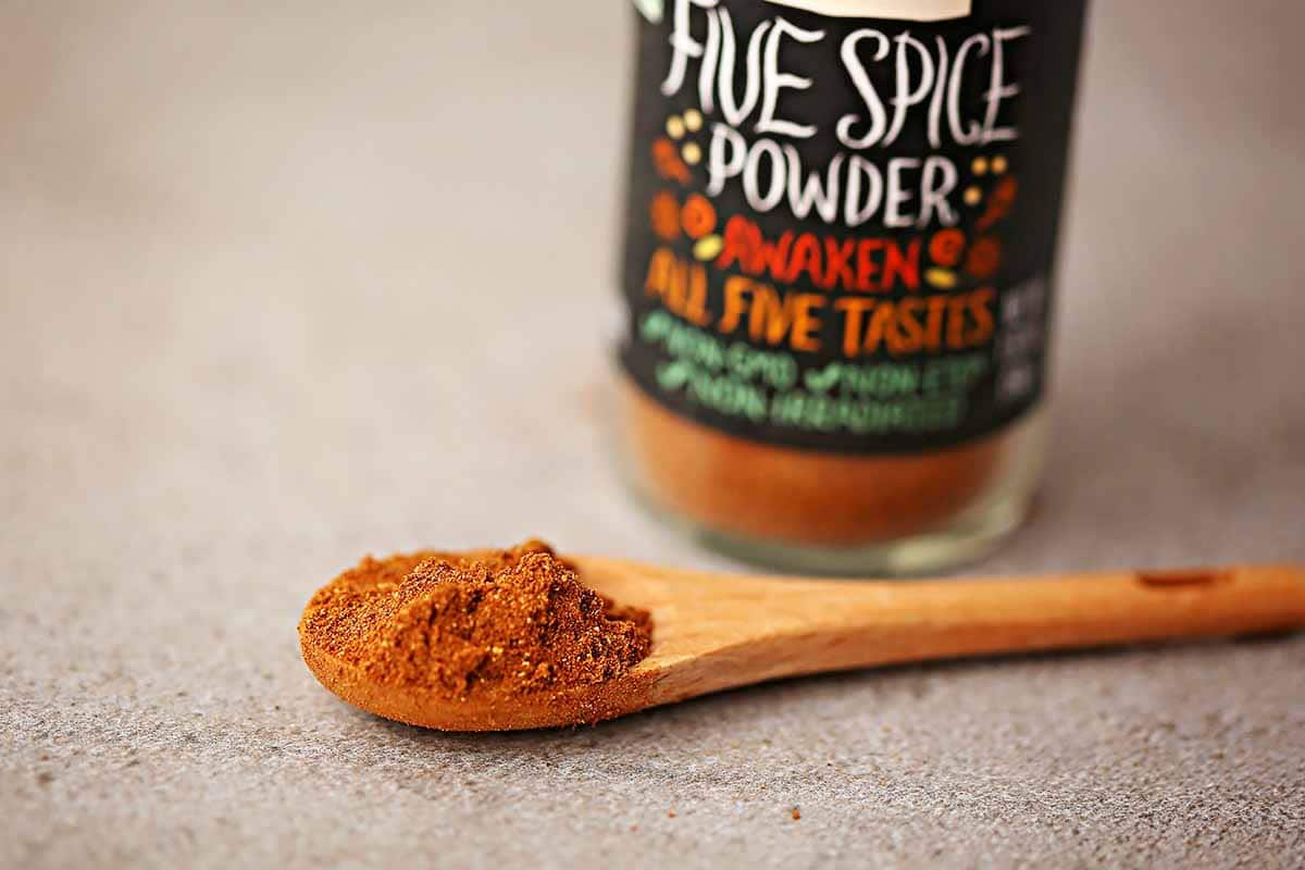 small wooden spoon filled with bright red-orange powdered spice with small glass bottle nearby labeled "five spice"
