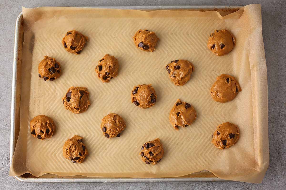 baking pan lined with parchment paper with unbaked drops of cookie dough