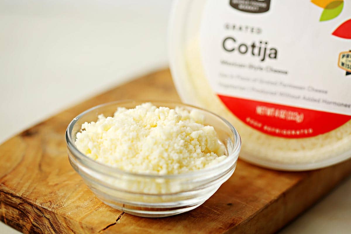 small glass dish filled with grated white cheese and round white container labeled "Cotija"