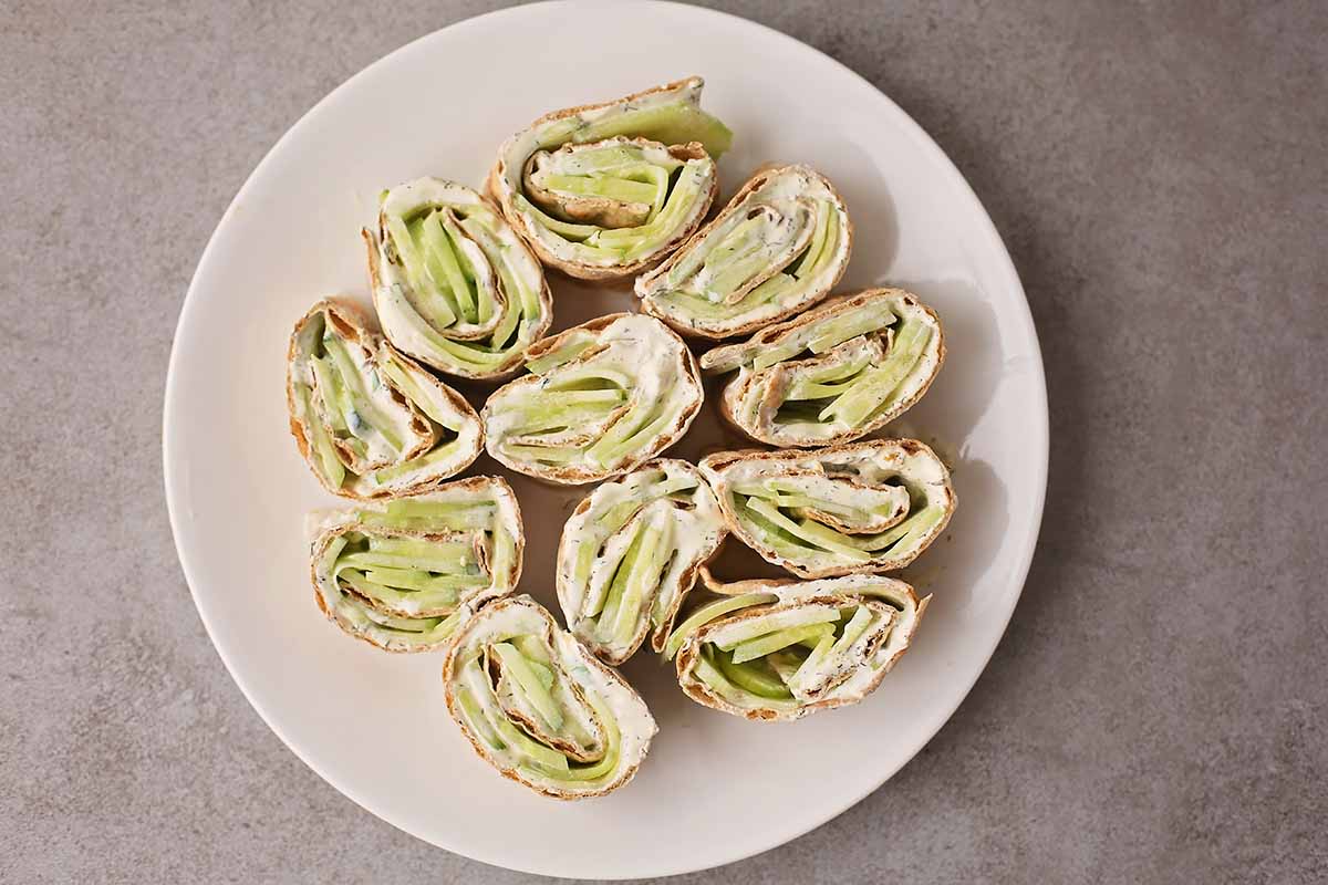 serving plate with sliced pinwheel sandwich filled with white cream cheese and green vegetable