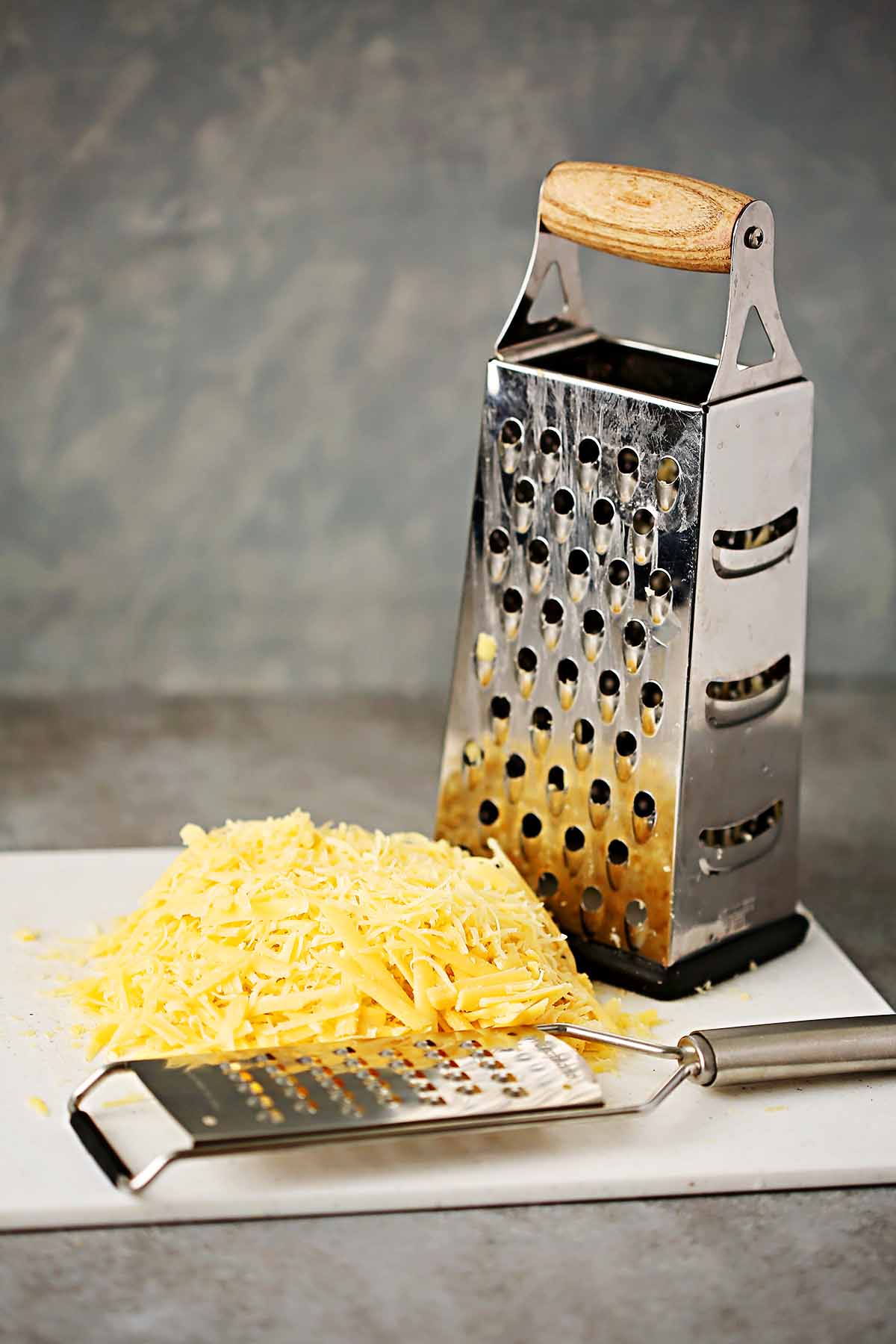 cutting board with grated cheese, box grater and a Microplane