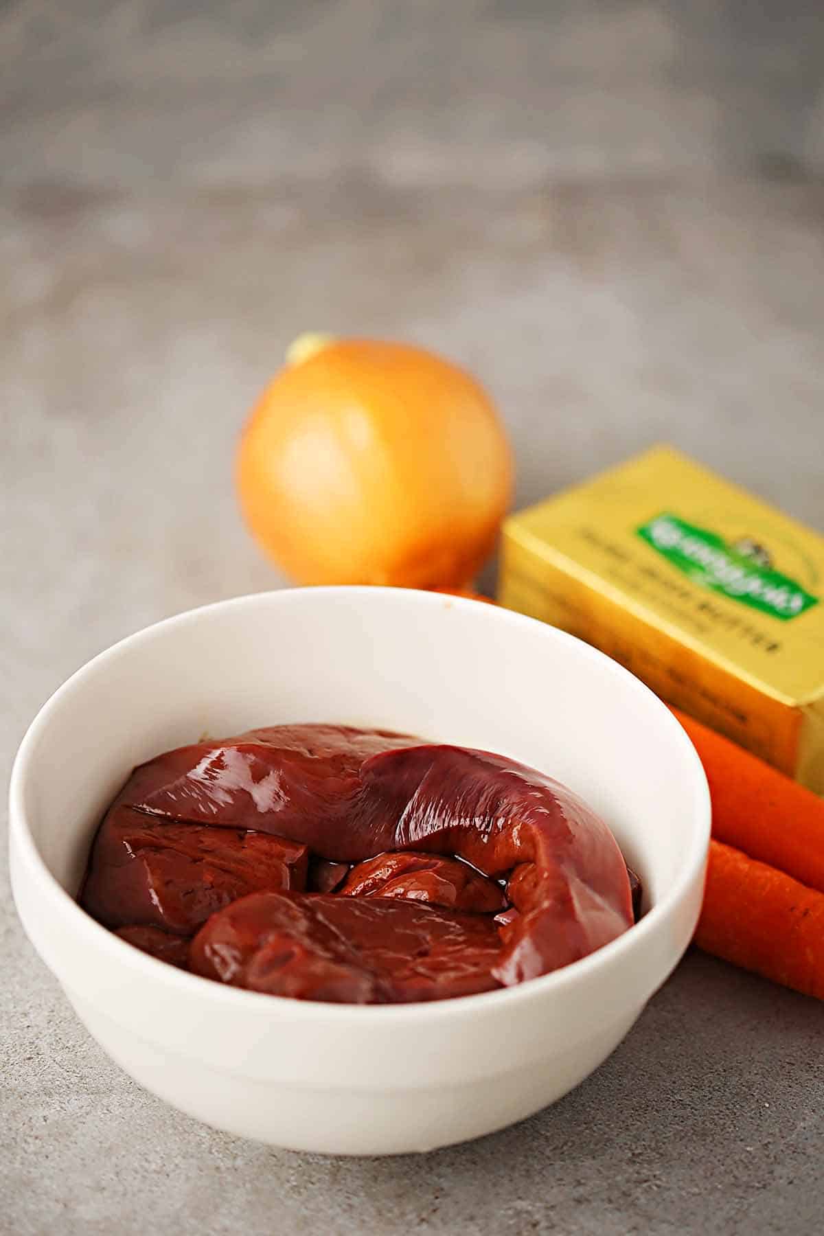 white bowl filled with raw liver pieces, big onion and block of butter