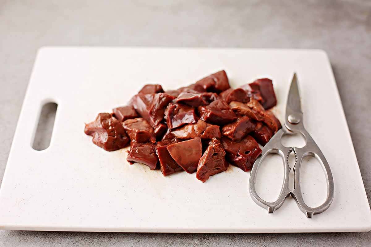 cutting board with sliced raw liver pieces and kitchen shears