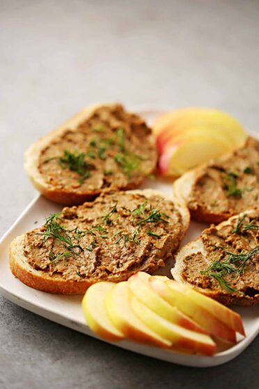 serving plate with bread slices topped with brown meaty spread and sliced apples