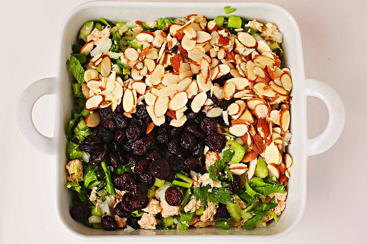 white dish with canned chicken chunks, dried cranberries, sliced almonds, diced celery and onion 