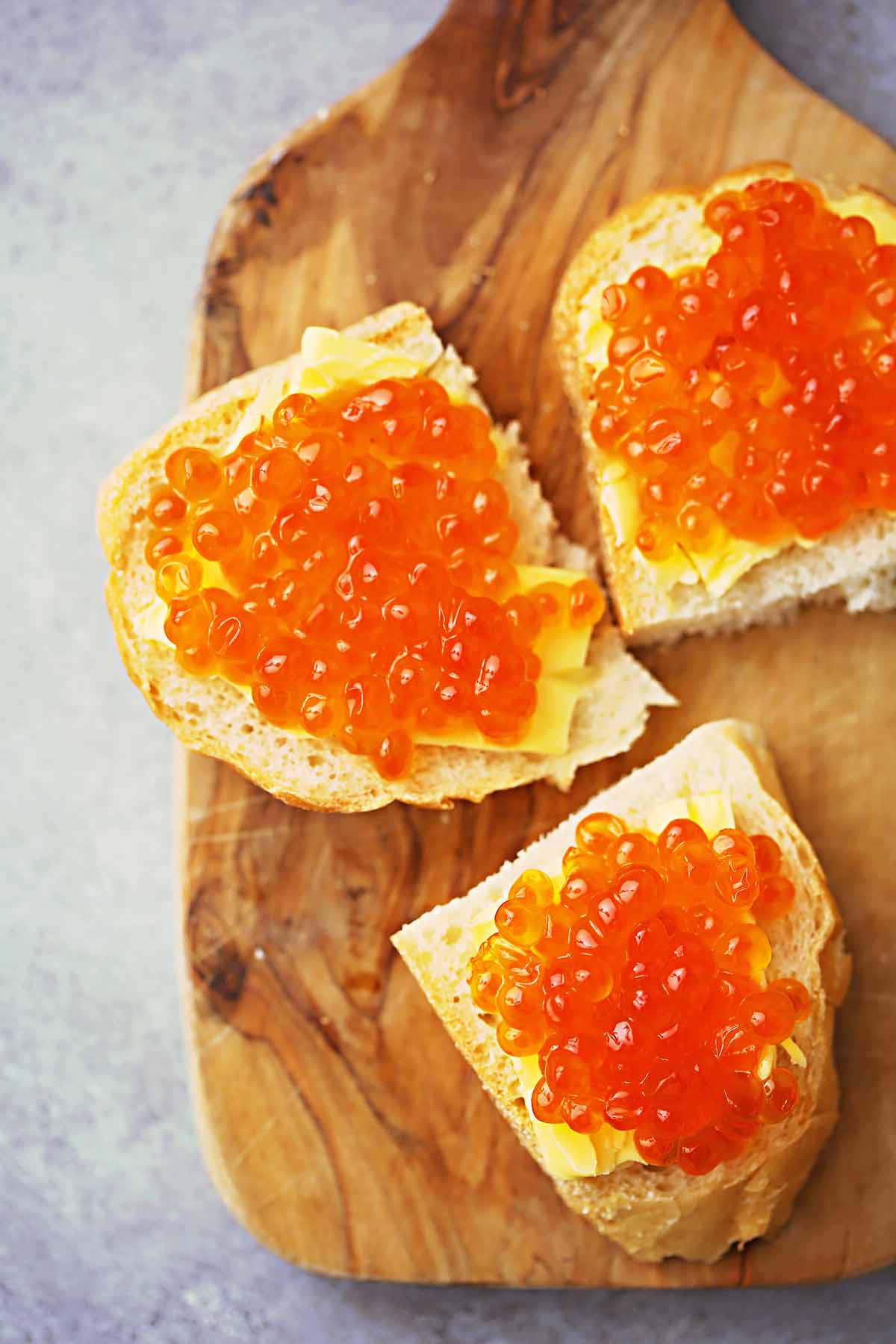 serving wooden board with small sandwiches with butter topped with fish caviar