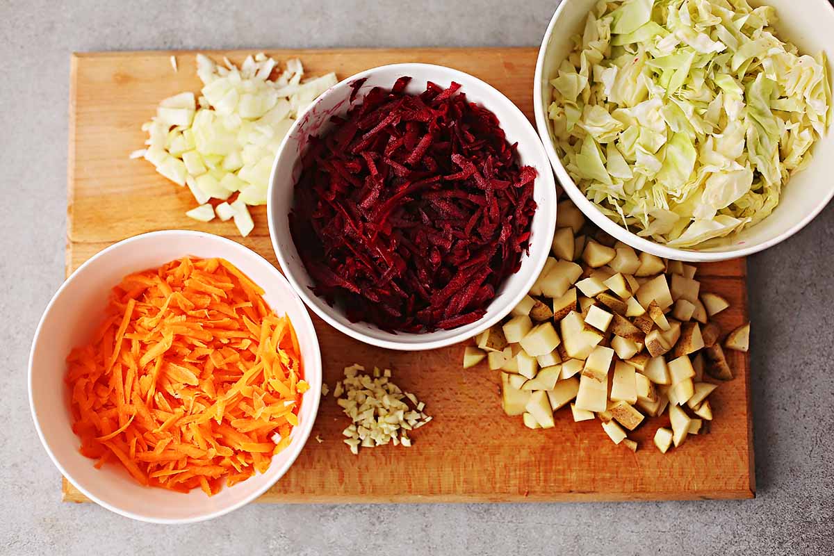 cutting board with chopped vegetables: potatoes, onions, carrots, beets, cabbage