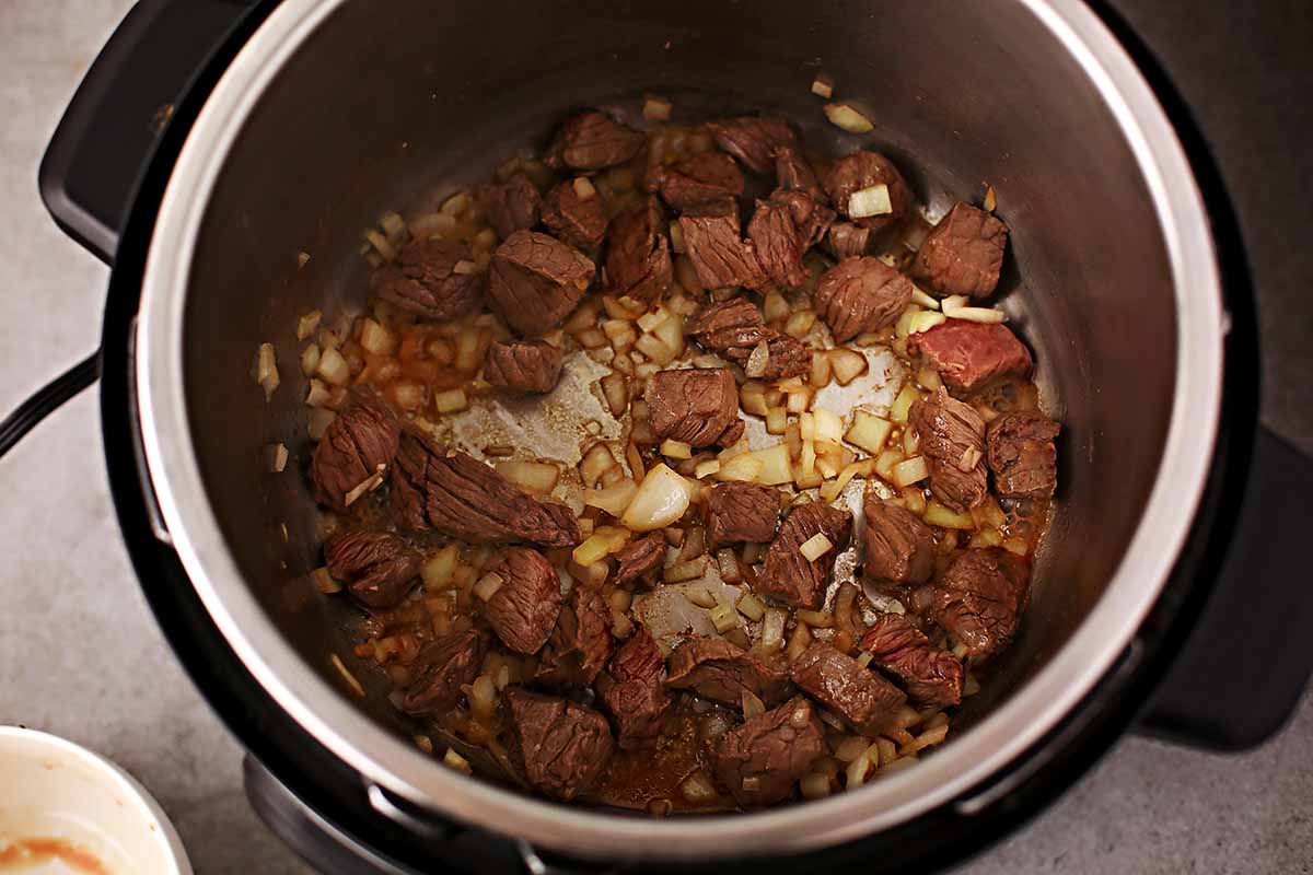 instant pot insert with beef stew meat and cooked diced onions
