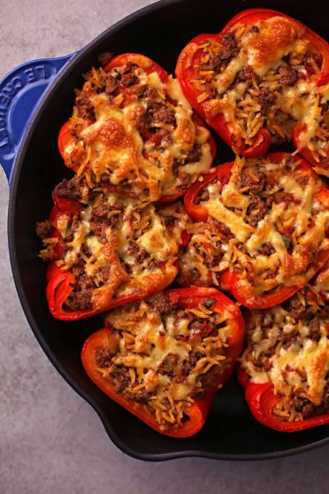 cast iron skillet filled with stuffed peppers topped with cheese