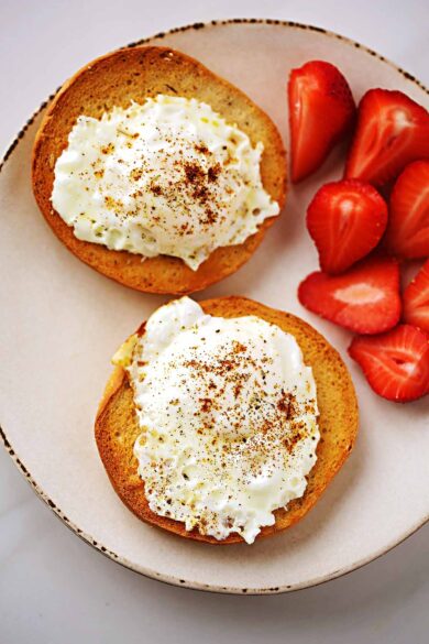 serving plate with sliced toasted bagel topped with fried egg and a side of sliced strawberries