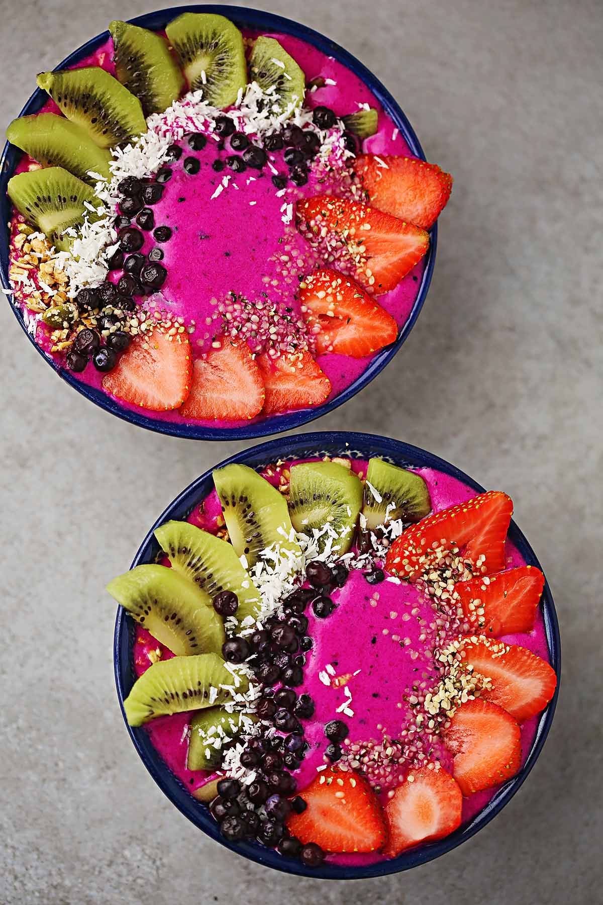 two serving bowls filled with pink pitaya smoothie and decorated with fresh fruits