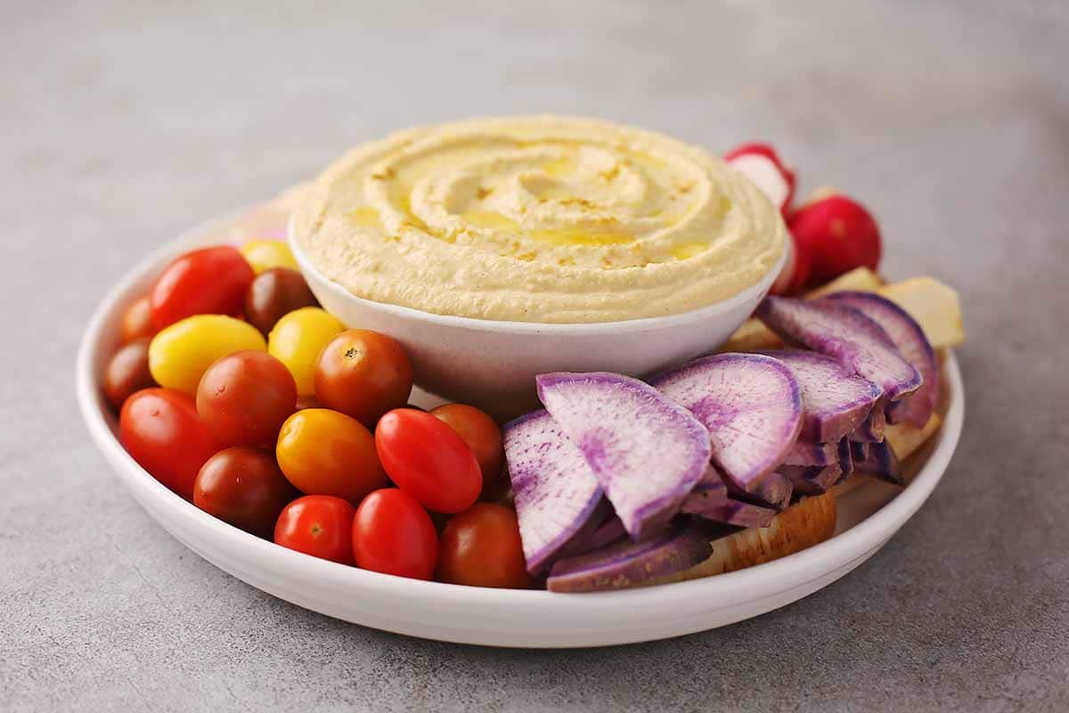 large plate with fresh sliced vegetables and dish with hummus 