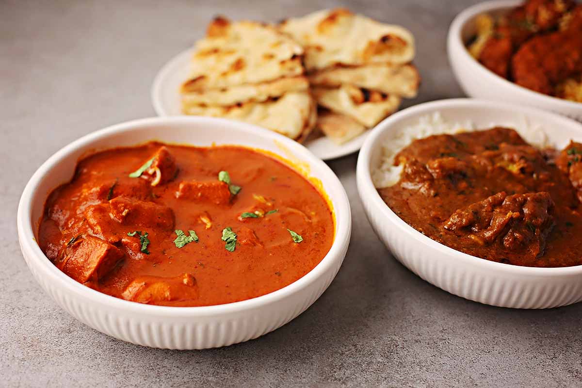 serving bowls filled with bright red tikka masala and butter chicken 