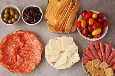table with plates filled with spuntini appetizers: salami, sliced cheese, olives, grape tomatoes, crackers