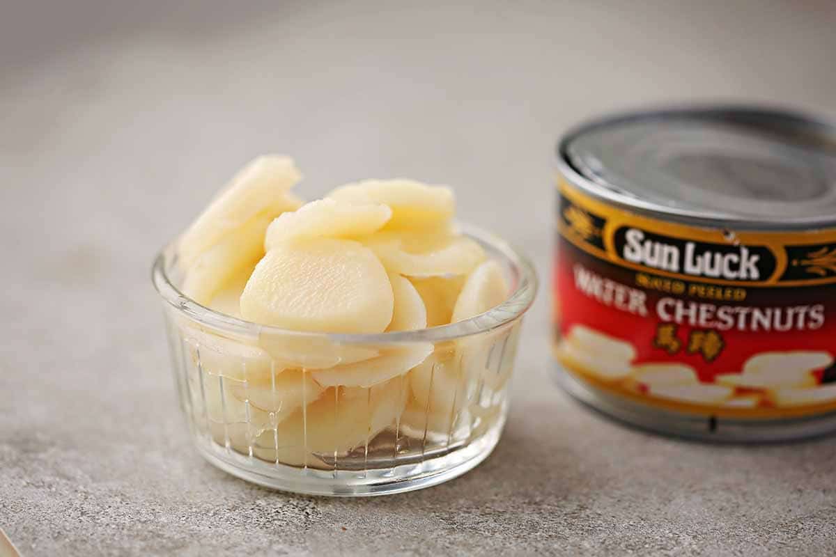 small glass bowl filled with sliced water chestnuts, can with label "chestnuts" next to it. 