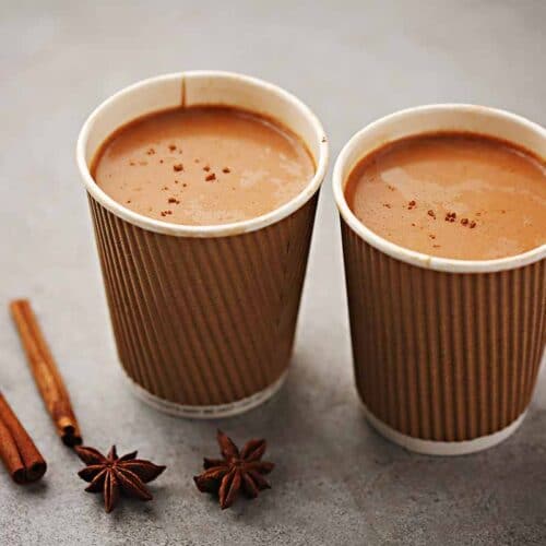 two cups filled with brown chai drink and spices
